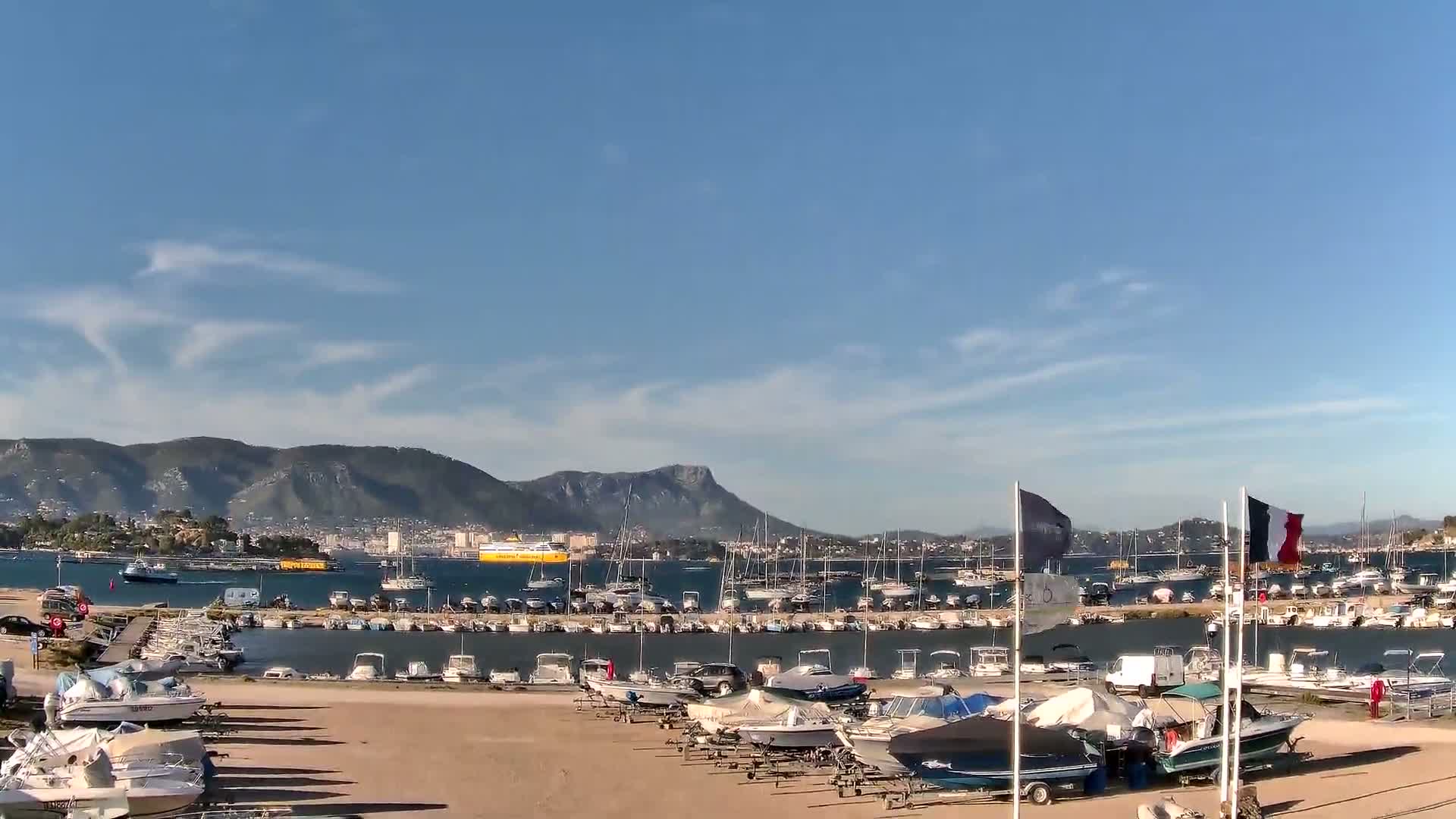 A harbor filled with numerous boats is nestled beside a hill under a cloudy sky.
