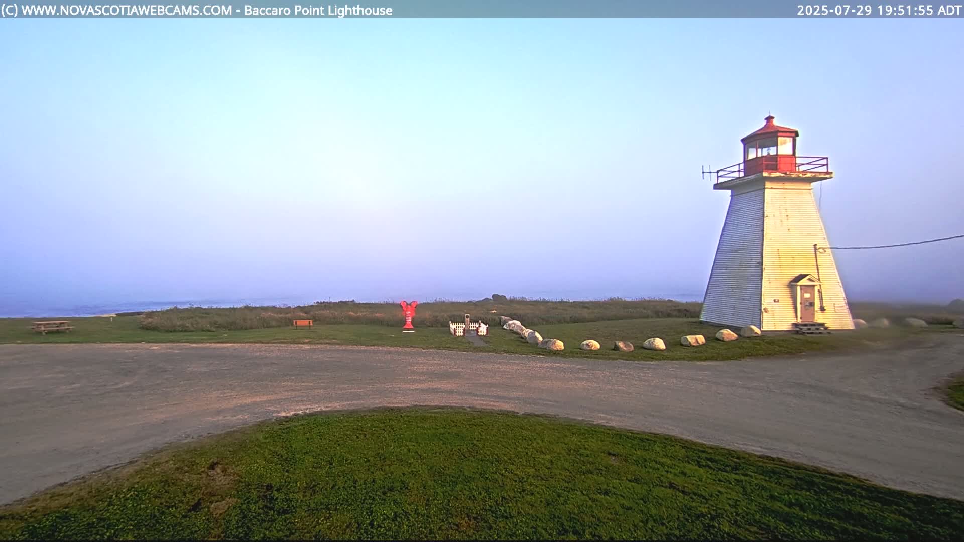 A lighthouse is visible in the distance on a dark, nighttime scene with grassy areas in the foreground.