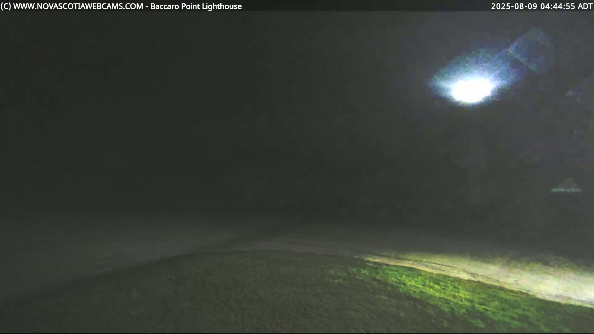 A bright light shines in a dark, foggy night sky above a low-lying expanse of dark green land.