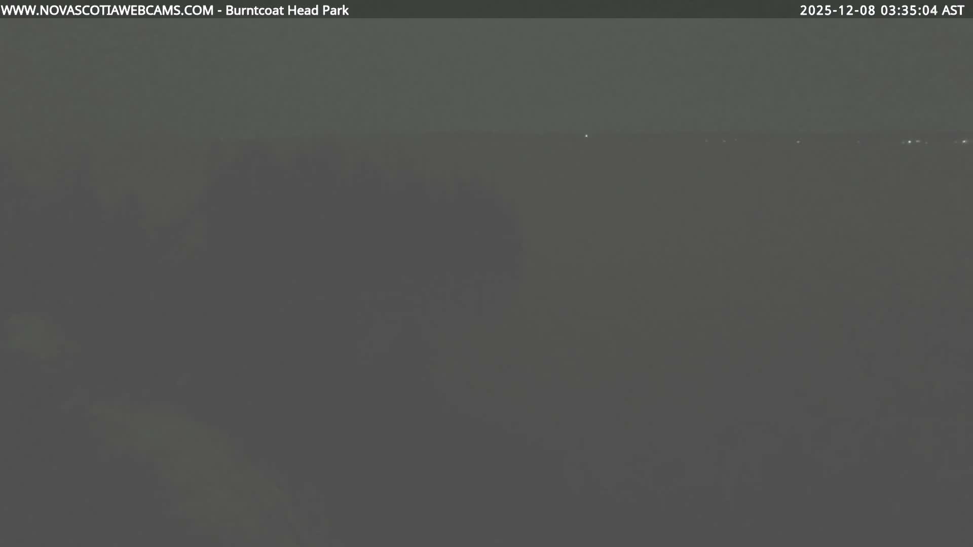 The image displays a very dark and indistinct outdoor scene at night, suggesting heavy overcast conditions or fog, with a few extremely faint distant lights barely visible in the upper right.