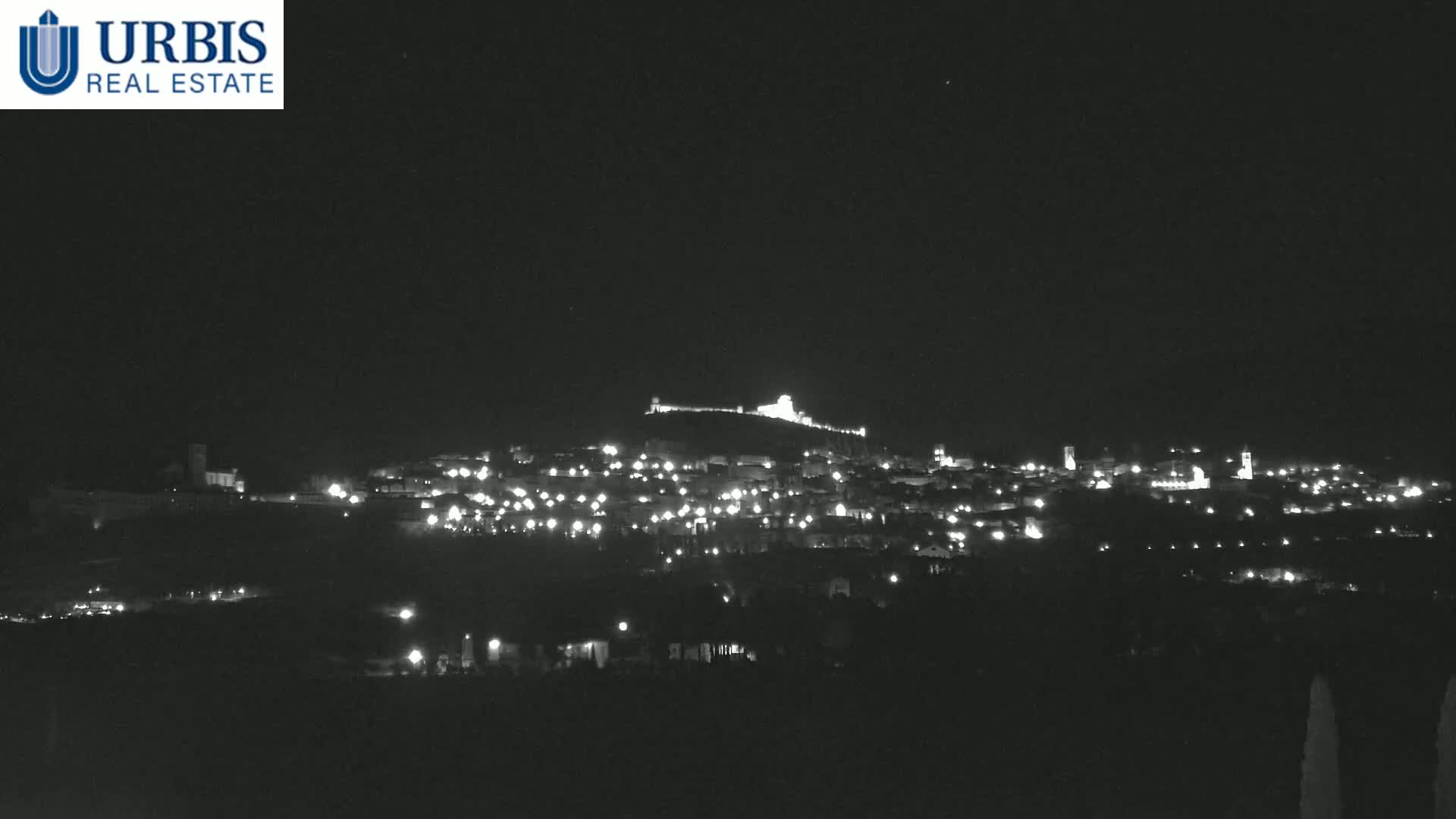 A hilltop town is illuminated at night under a clear, dark sky.