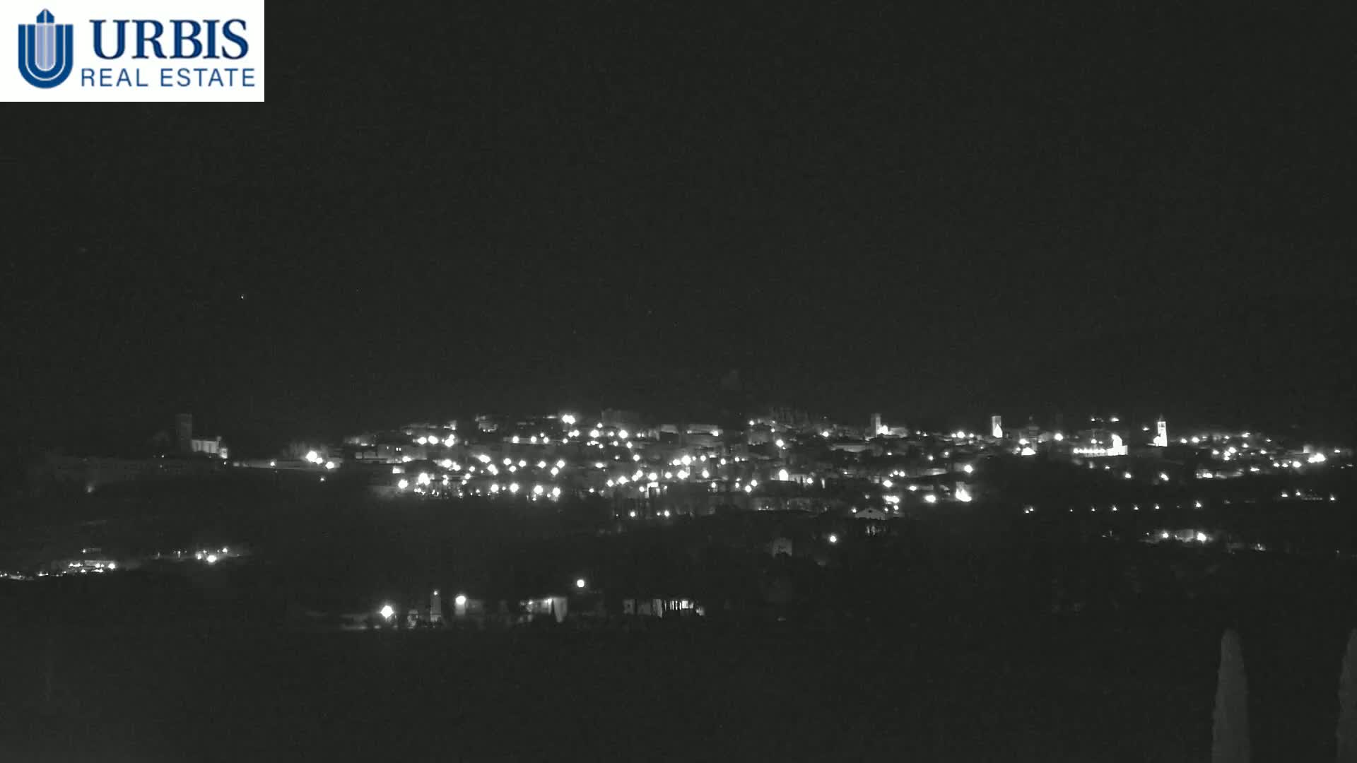 A nighttime long shot shows a small town's lights spread across a hill under a clear, dark sky.
