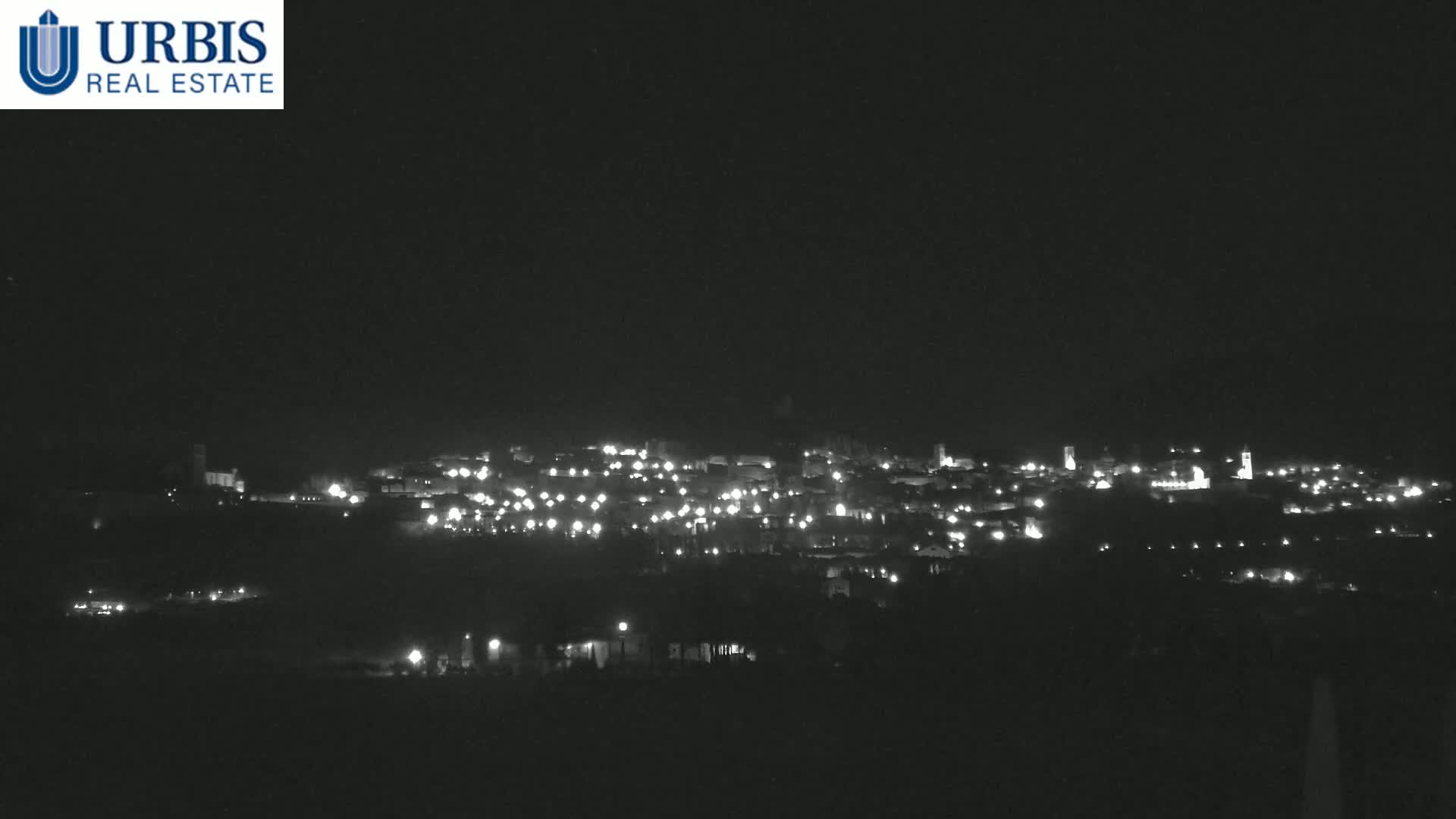 A nighttime long shot shows a small town's lights scattered across a hillside under a clear, dark sky.