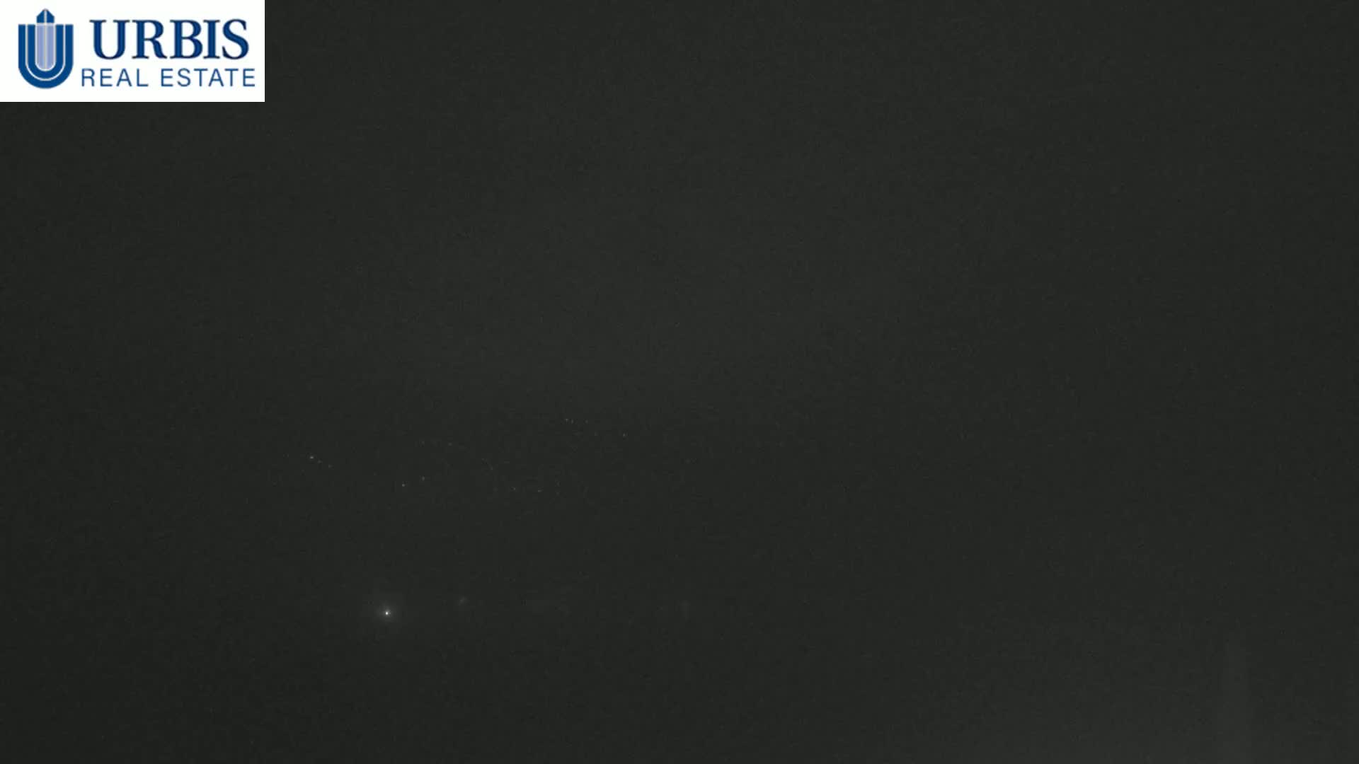 A dark, nighttime scene shows a few faint lights in the distance under an overcast sky.