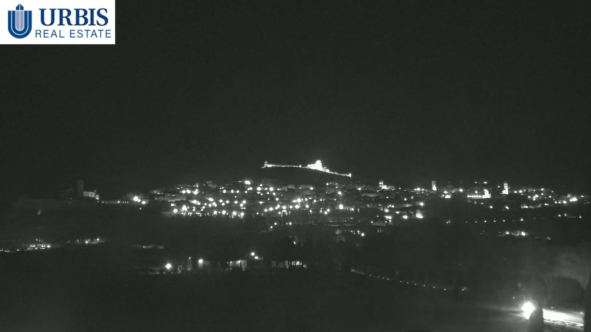 A hilltop town is illuminated at night under a clear, dark sky.