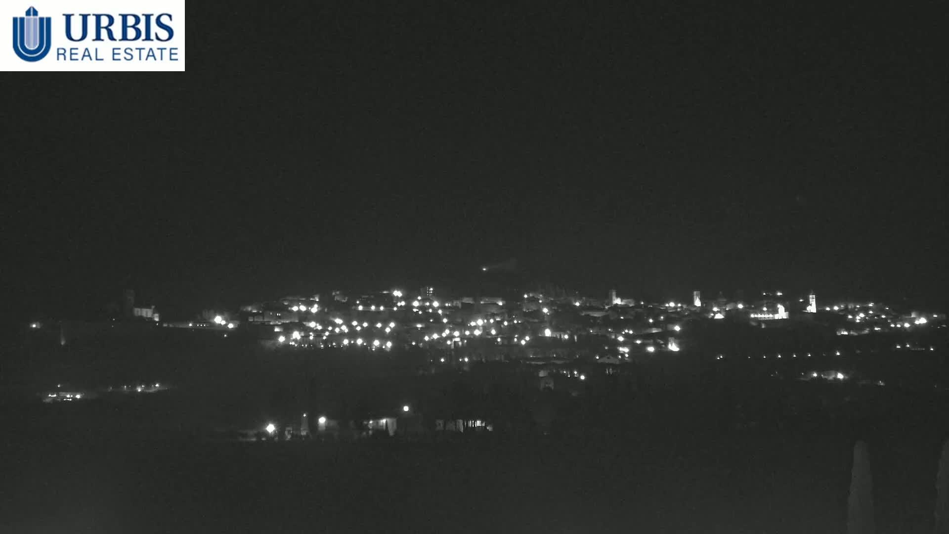 A nighttime long shot shows a small town’s lights scattered across a hillside under a clear, dark sky.