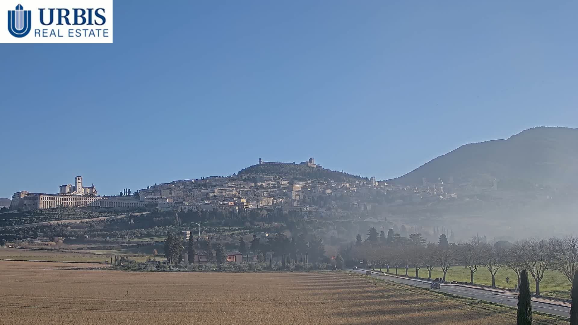 A hilltop town, partially obscured by fog, is visible in the distance under a clear blue sky.