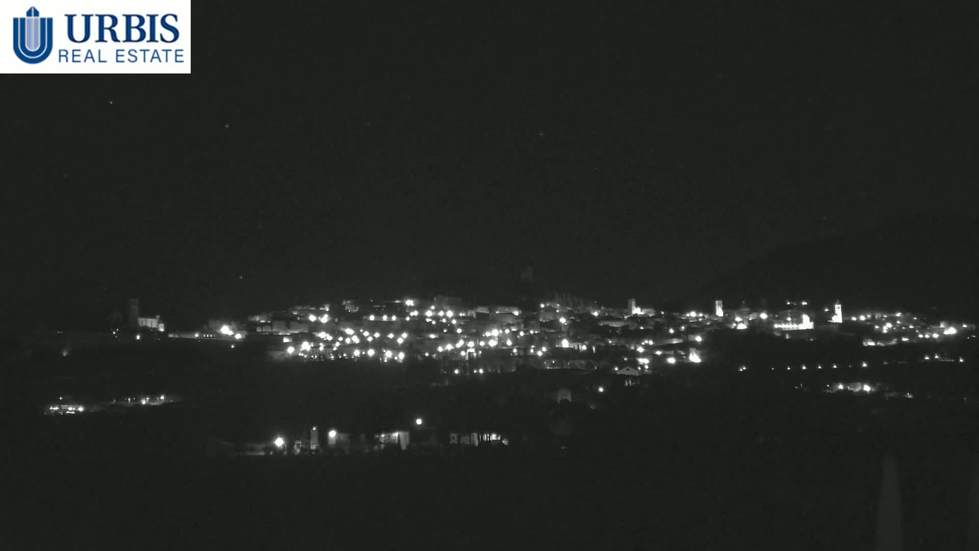 A nighttime long shot of a town's illuminated buildings spread across a hill.