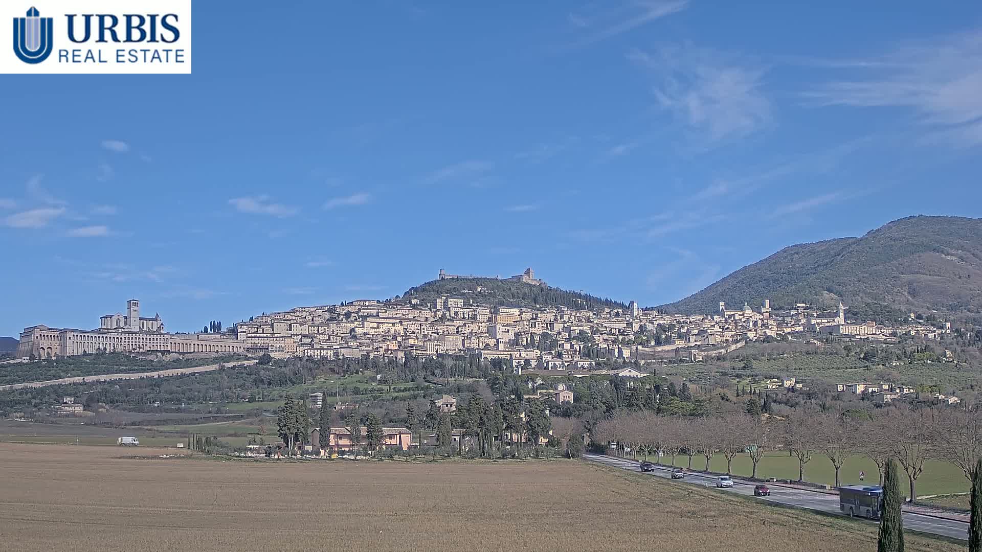 A large hilltop town, with a large basilica, is seen in the distance under a clear blue sky.