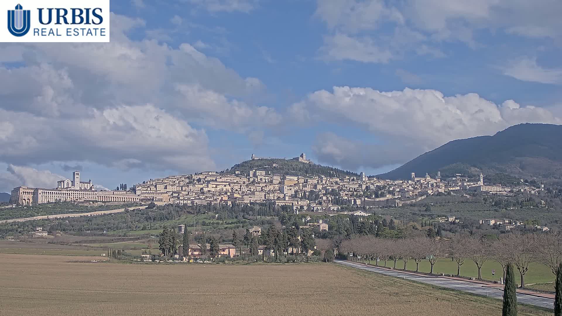 A hilltop town, nestled between mountains, is visible under a partly cloudy sky.