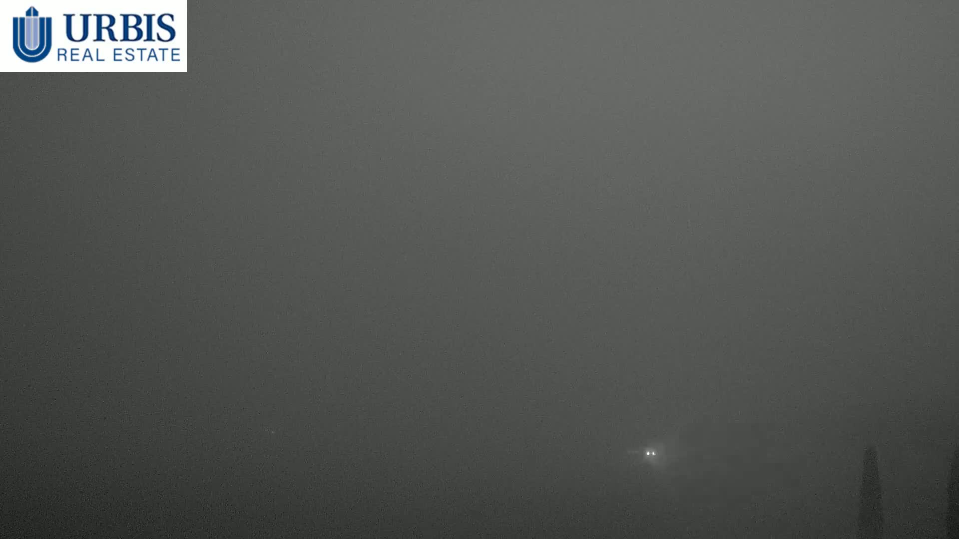 A vehicle's headlights are barely visible through heavy fog.