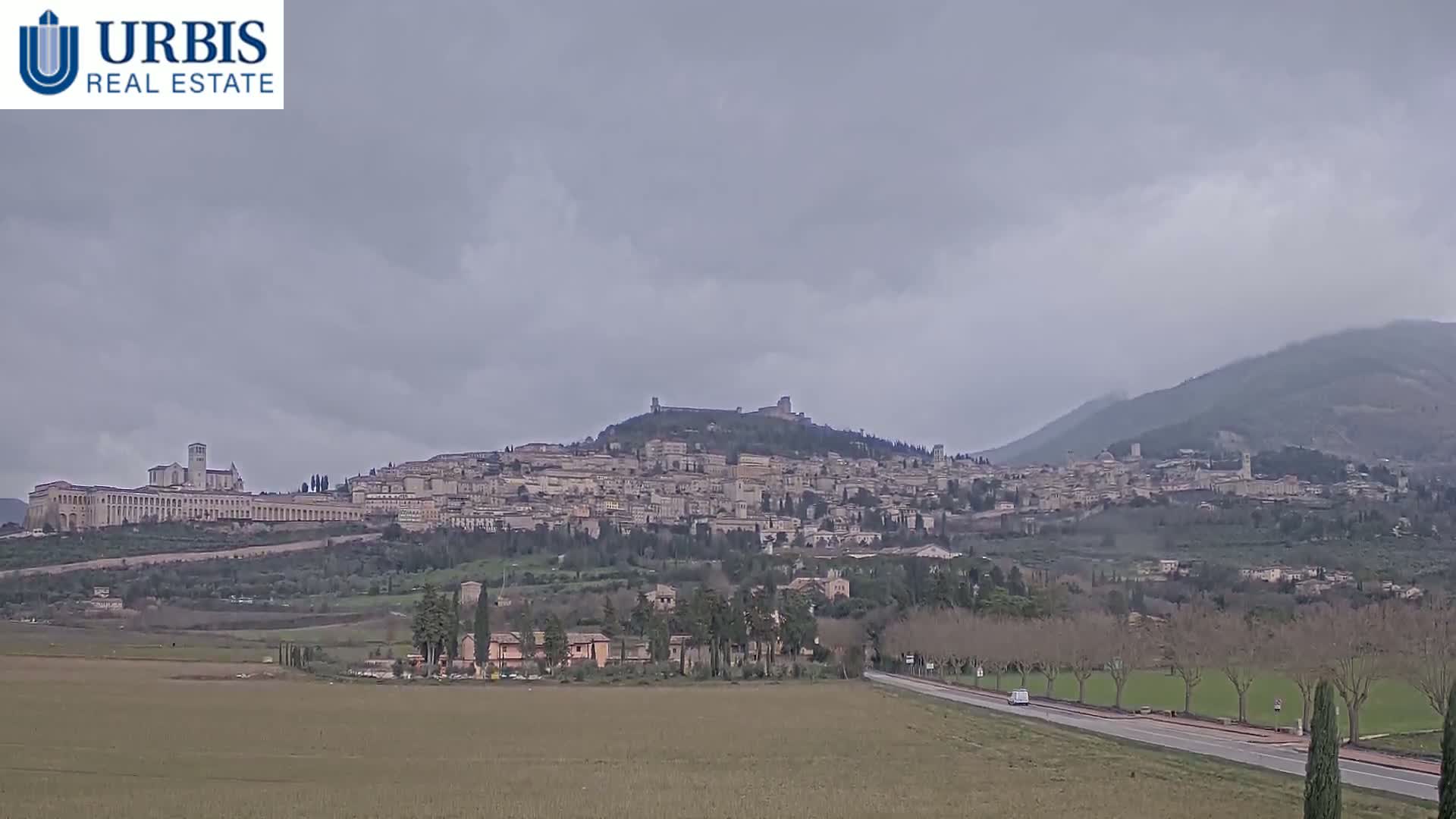 A large hilltop town is visible under an overcast sky, with a flat, sparsely vegetated plain stretching to the foreground.