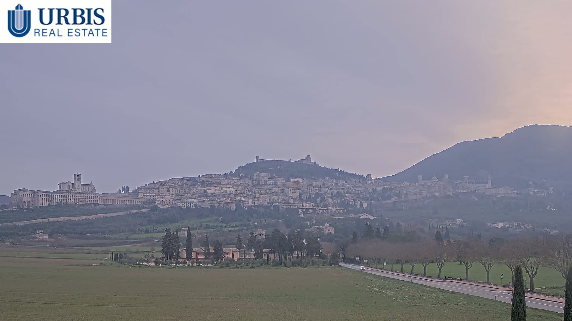 A hazy, distant view of Assisi, Italy, nestled in a valley between hills.