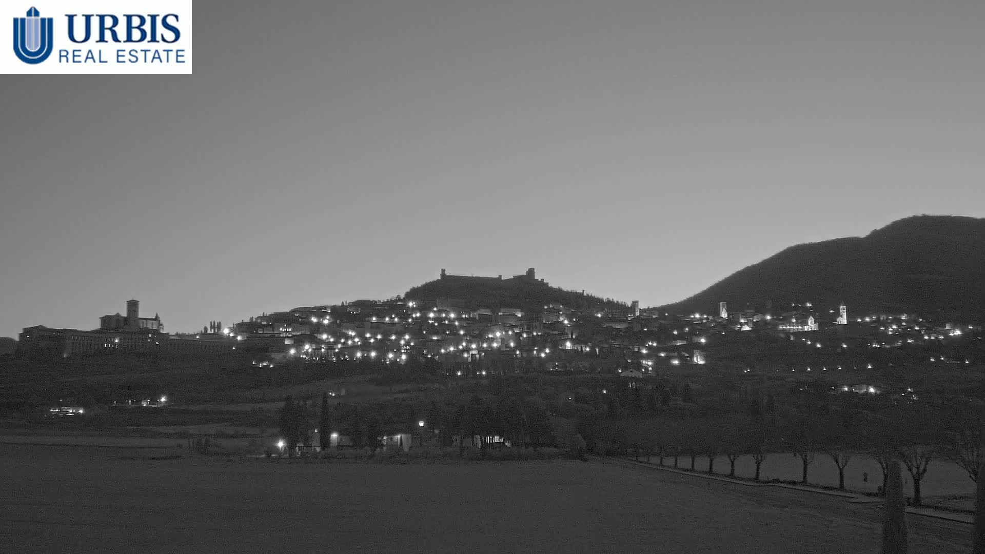 A hilltop town is illuminated at twilight under a dusky sky.