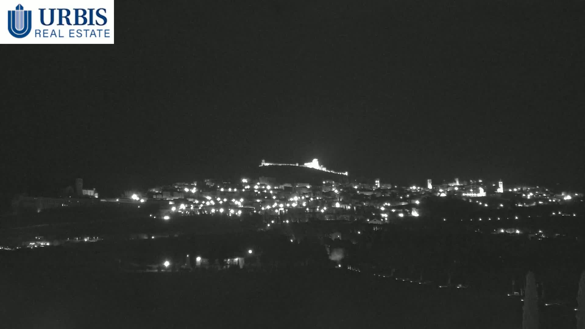 A nighttime, long shot of a hilltop town illuminated by many small lights, with a structure atop the hill.