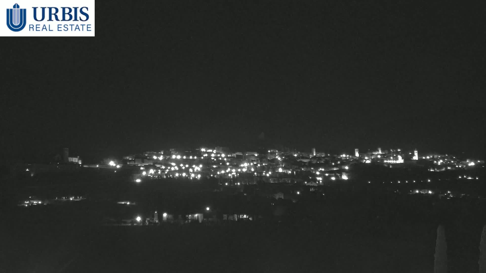 A nighttime long shot of a town illuminated by scattered lights against a dark sky.