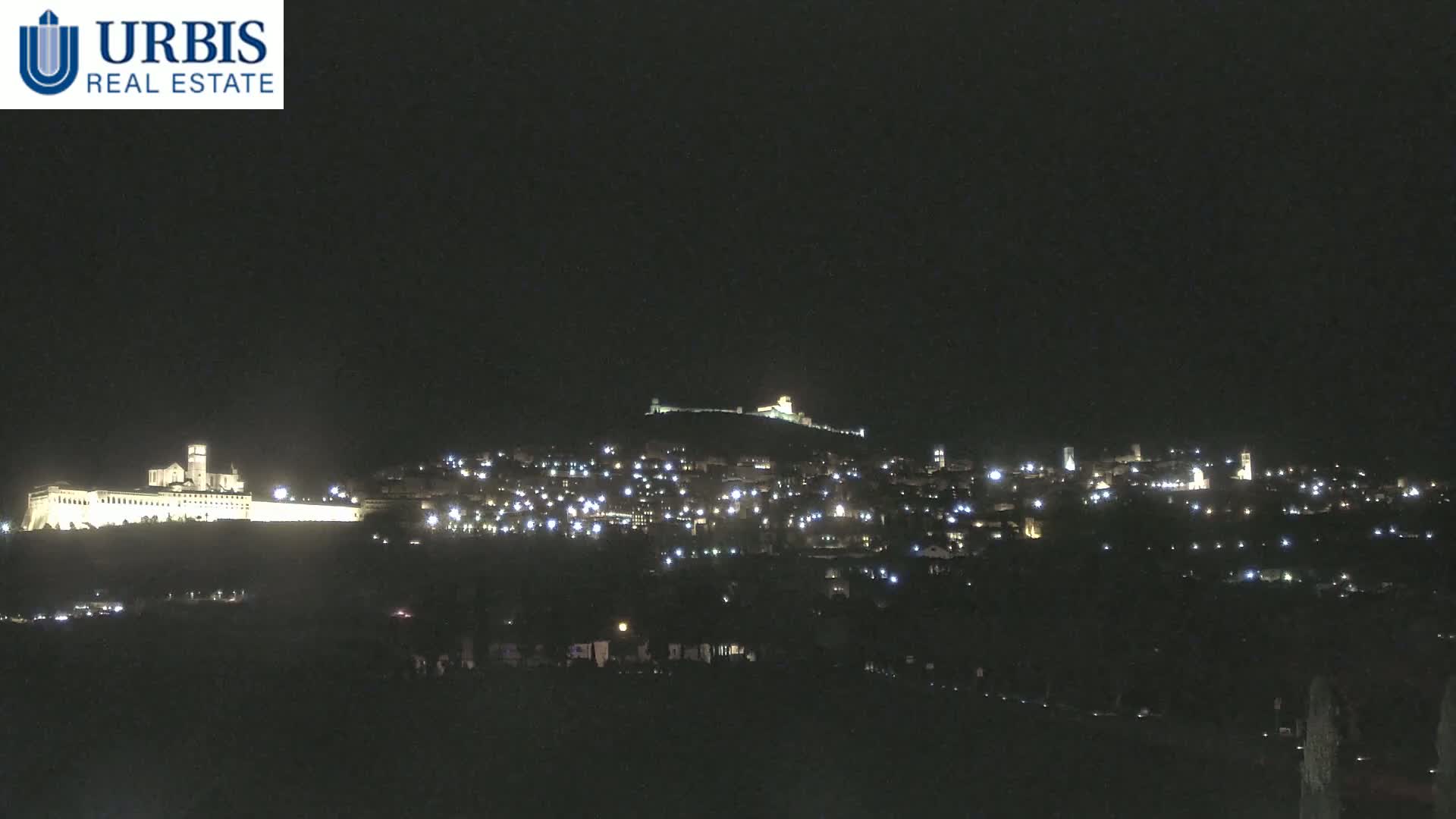 A nighttime view of a town and hilltop structures illuminated by lights under a dark, clear sky.