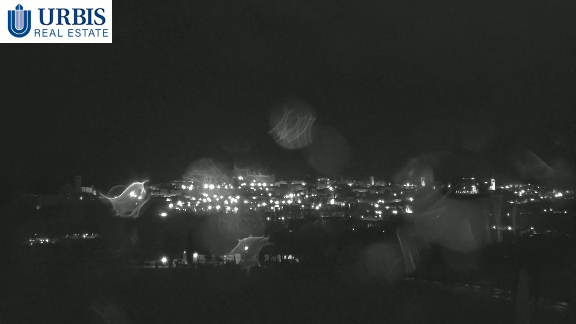 A nighttime view of a town's lights, seen through a rain-streaked window.