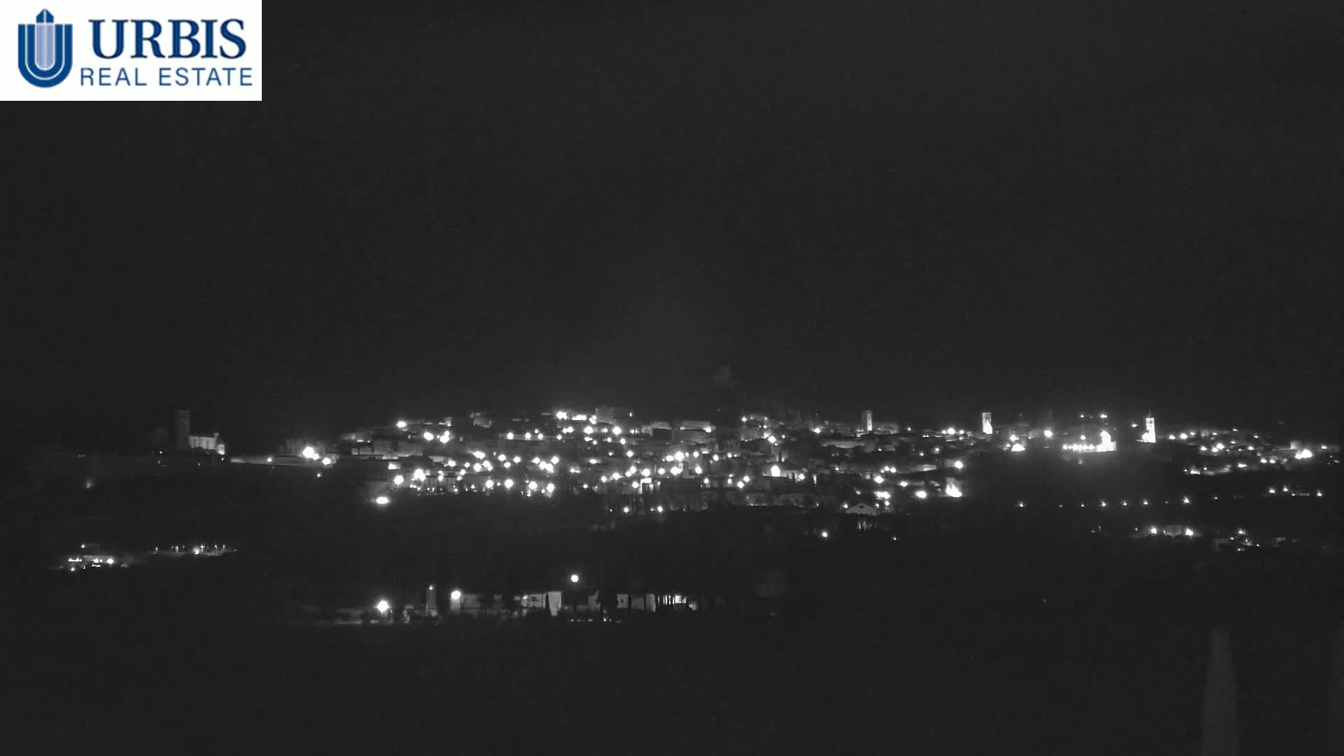 A nighttime long shot of a town illuminated by scattered lights against a dark sky.