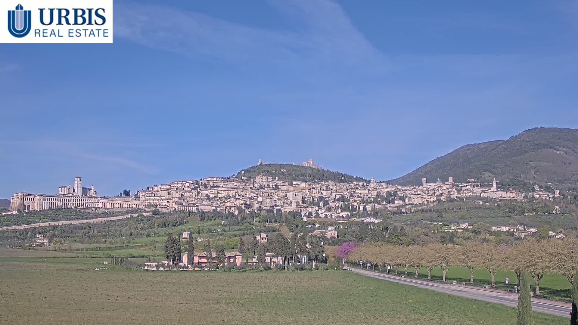 A large hill town, nestled between two mountains, is visible under a clear blue sky.