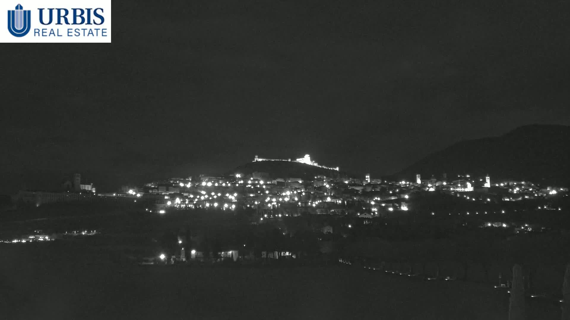 A nighttime view of a hilltop town illuminated by scattered lights, under a dark, clear sky.