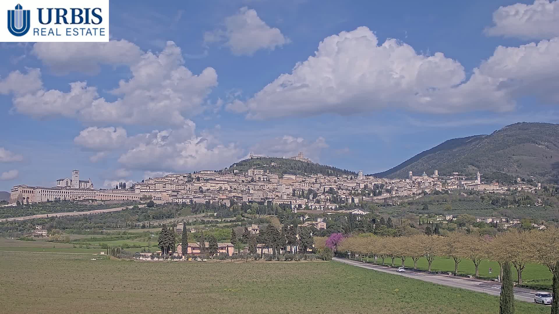 A hilltop town, nestled amongst rolling green hills under a partly cloudy sky, is visible from a distance.