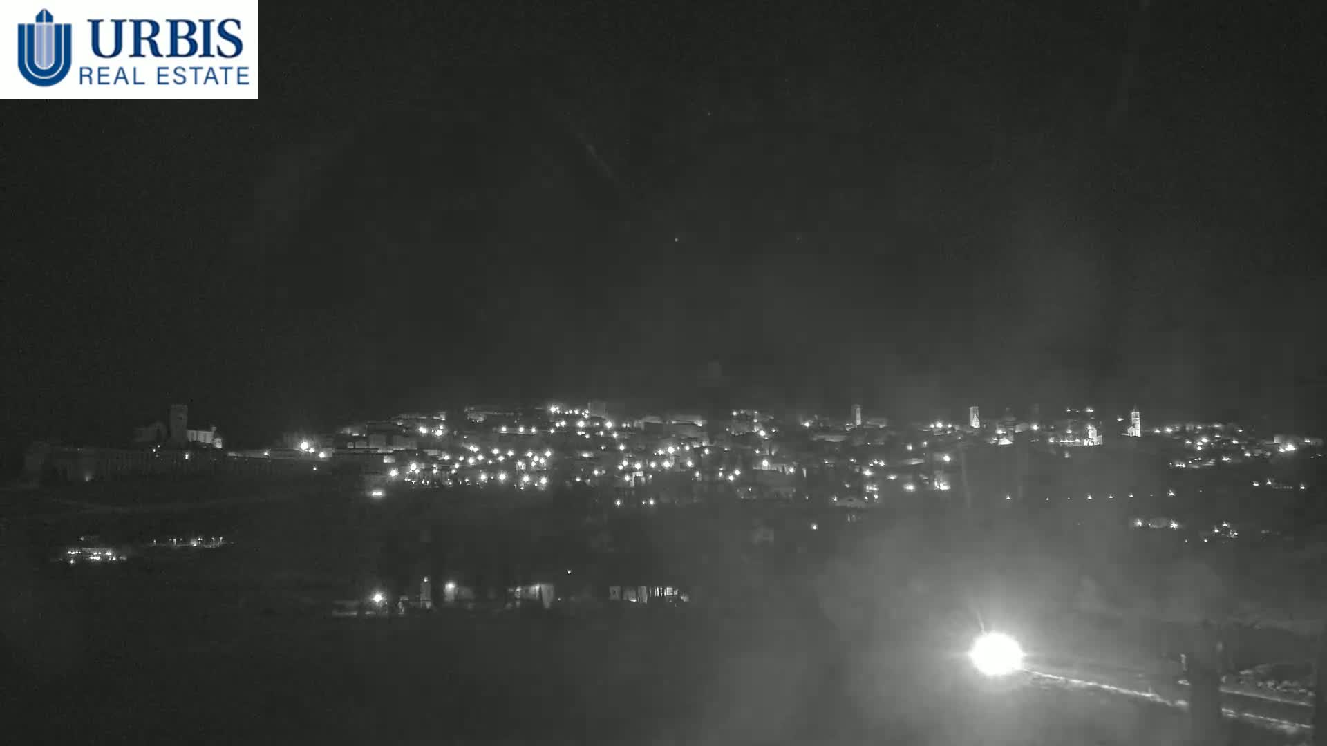 A nighttime long shot shows a small town illuminated with scattered lights under a dark, hazy sky.