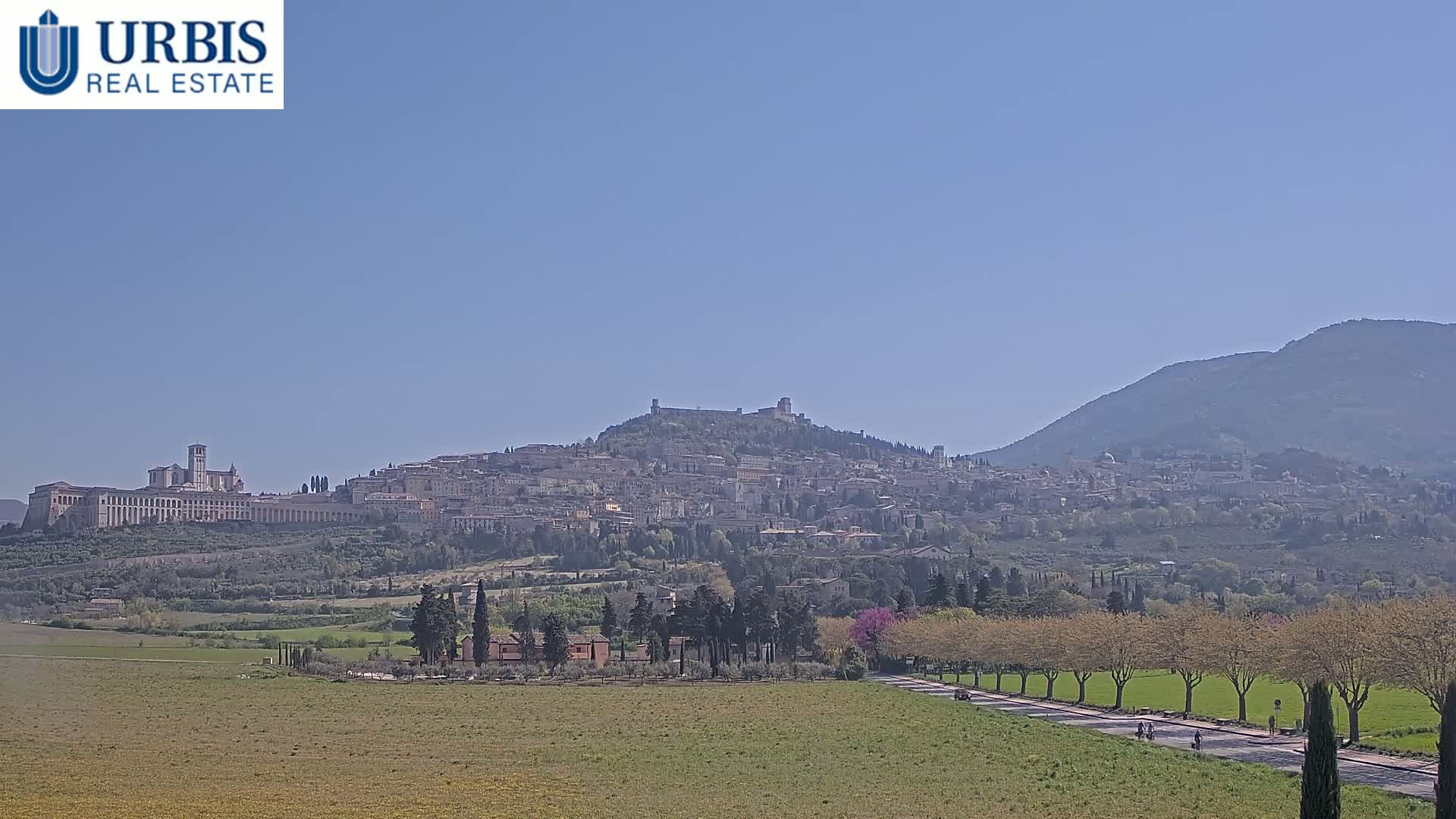 A hilltop town with a large basilica, nestled among rolling hills under a clear blue sky.