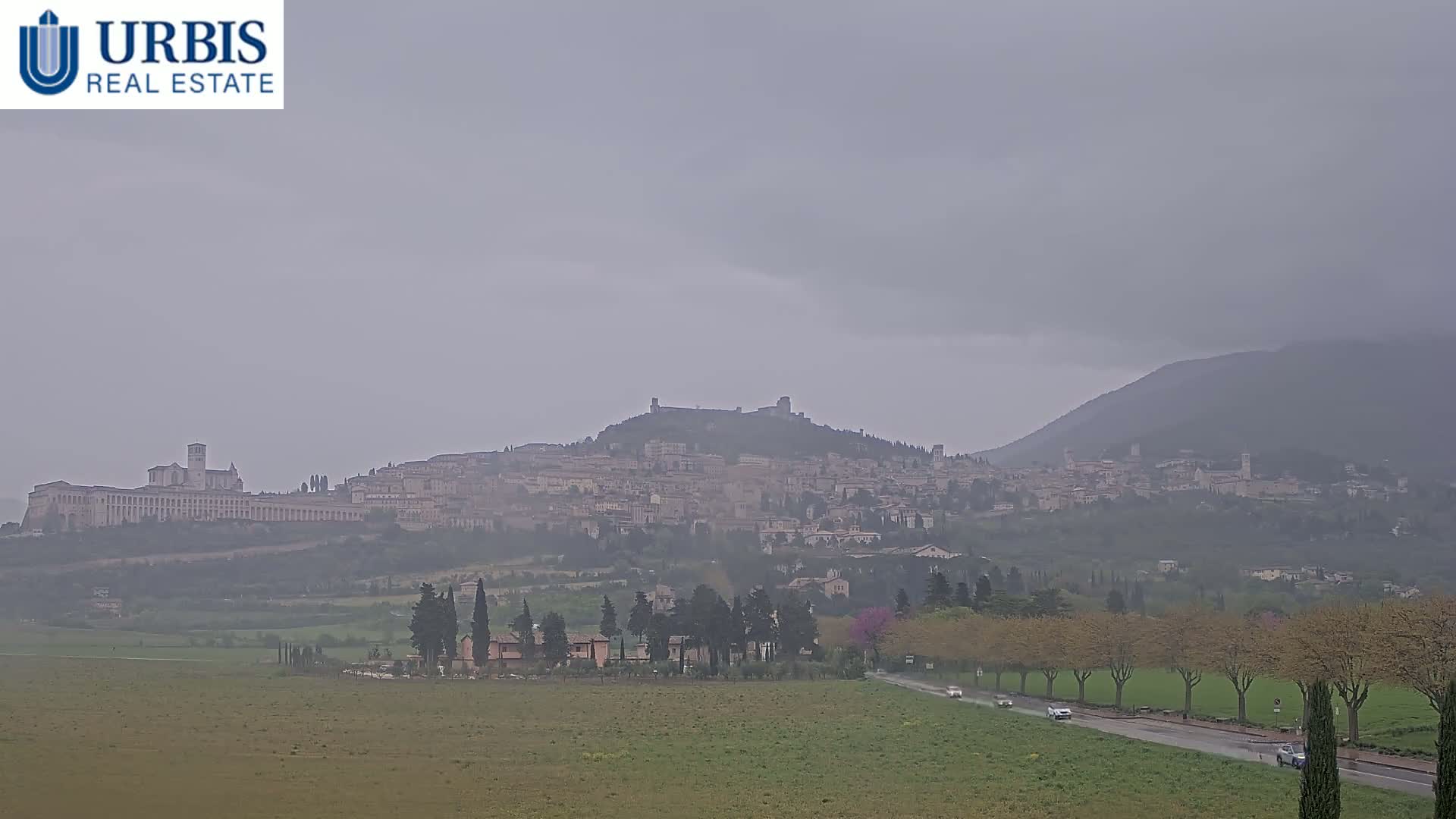 A hazy, overcast day reveals a hilltop town with buildings and structures nestled among the landscape, in the distance a mountain rises.