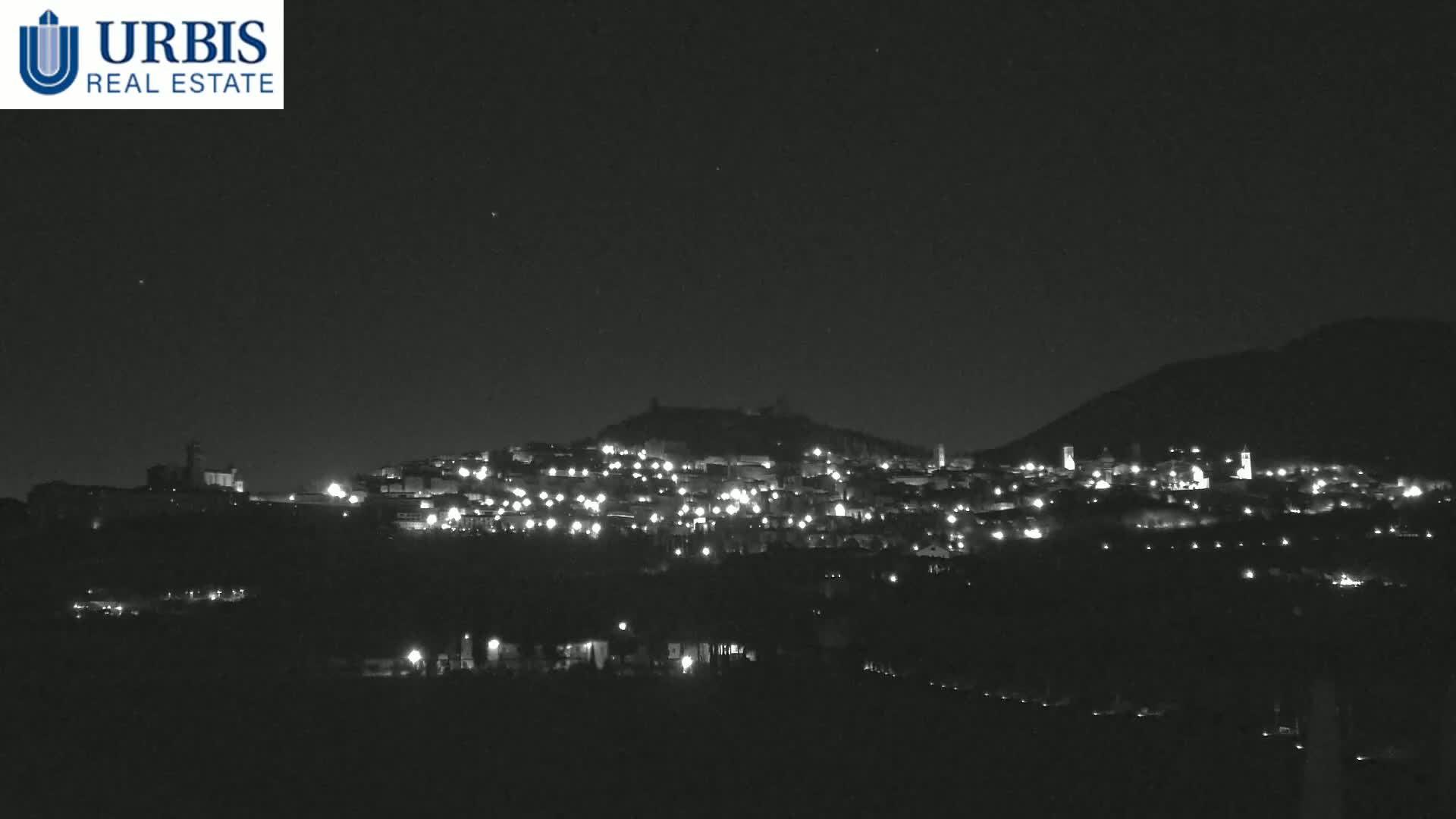 A nighttime view of a hilltop town illuminated by scattered lights under a clear, dark sky.
