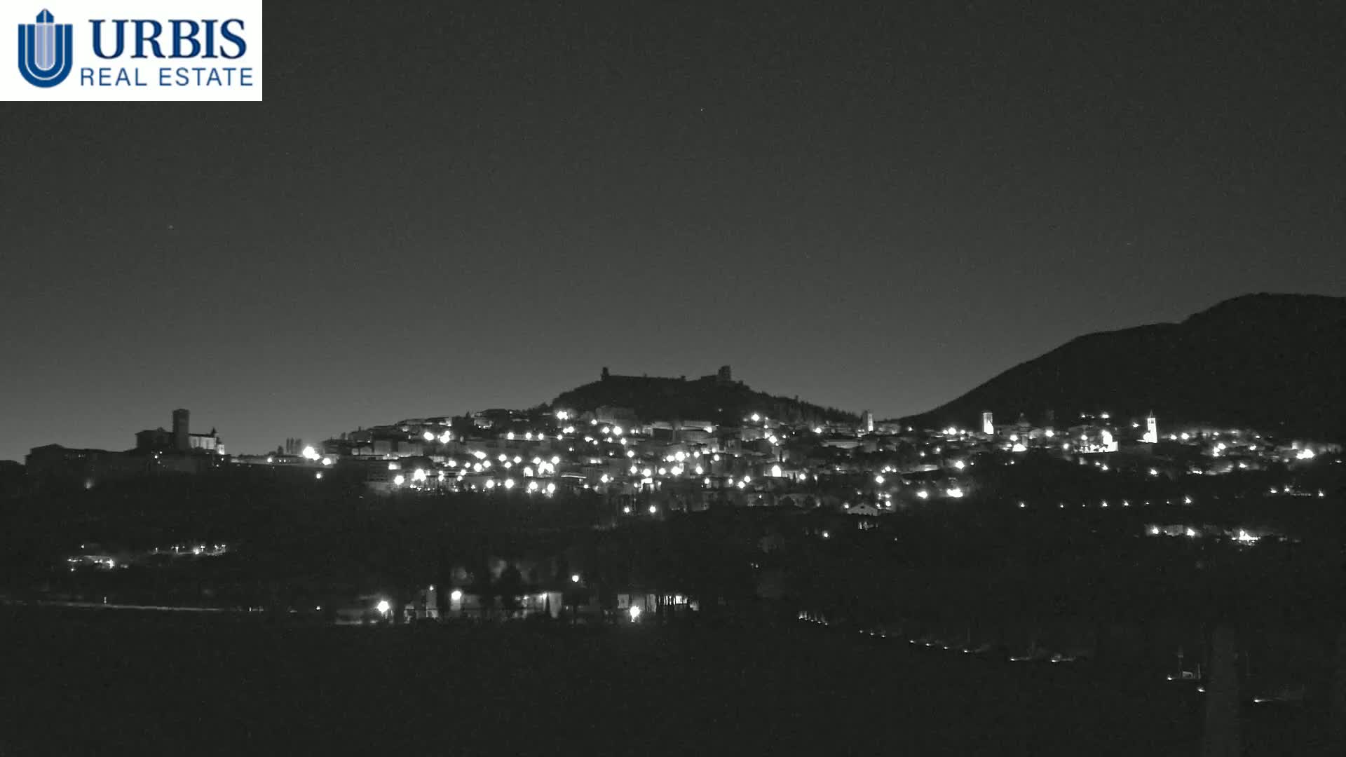 A nighttime view of a hilltop town illuminated by scattered lights, under a dark, clear sky.