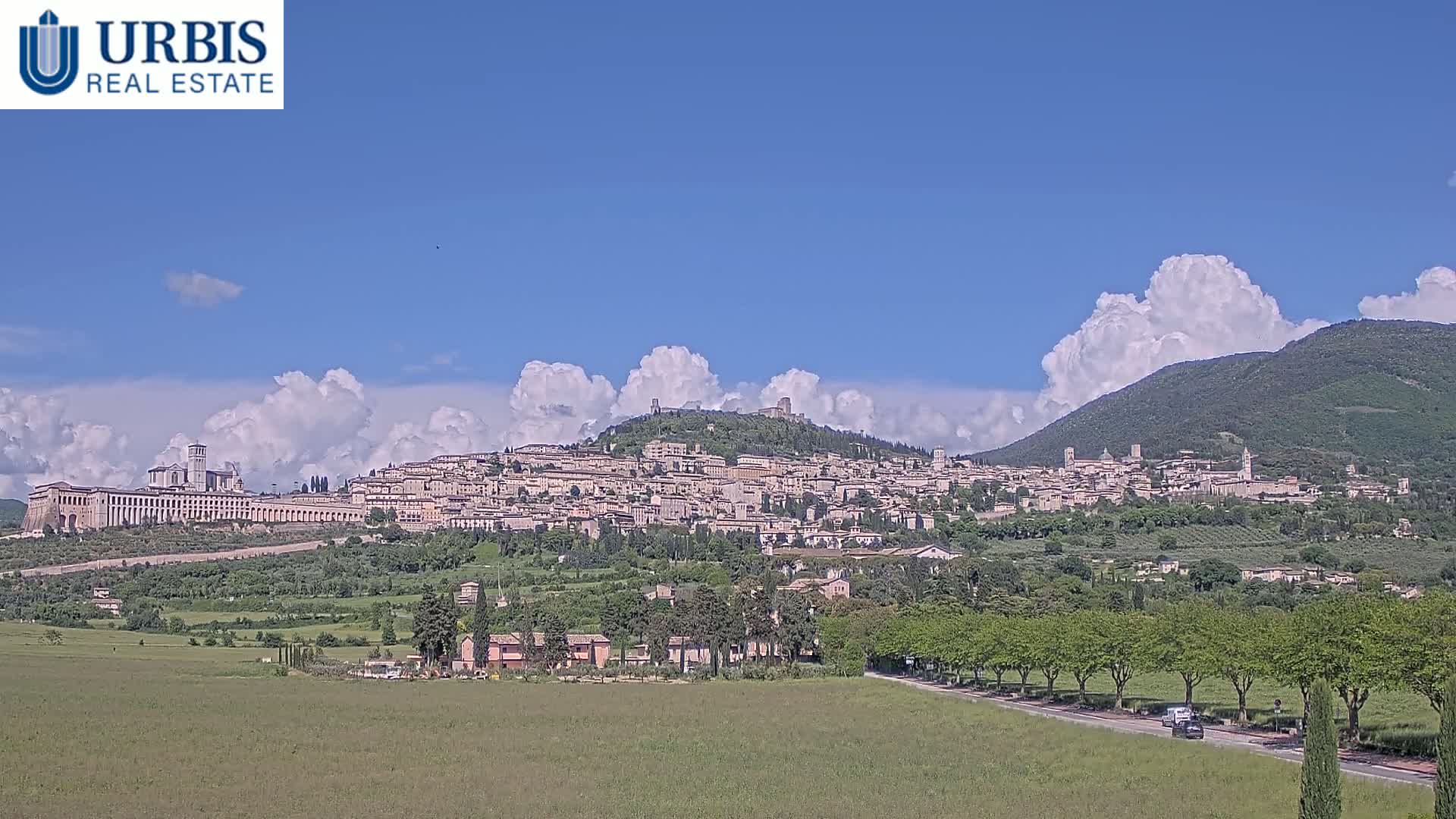 A large hill town is visible under a partly cloudy sky, with green fields and trees in the foreground.