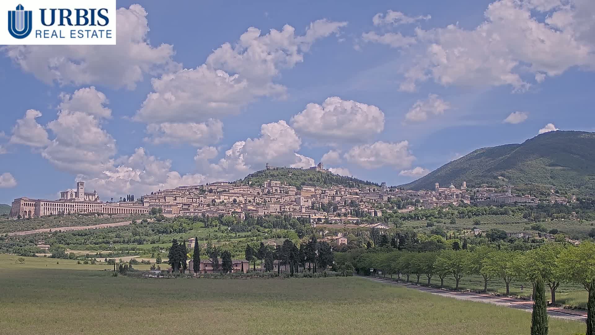 A large hilltop town with a large basilica sits beneath a partly cloudy sky.