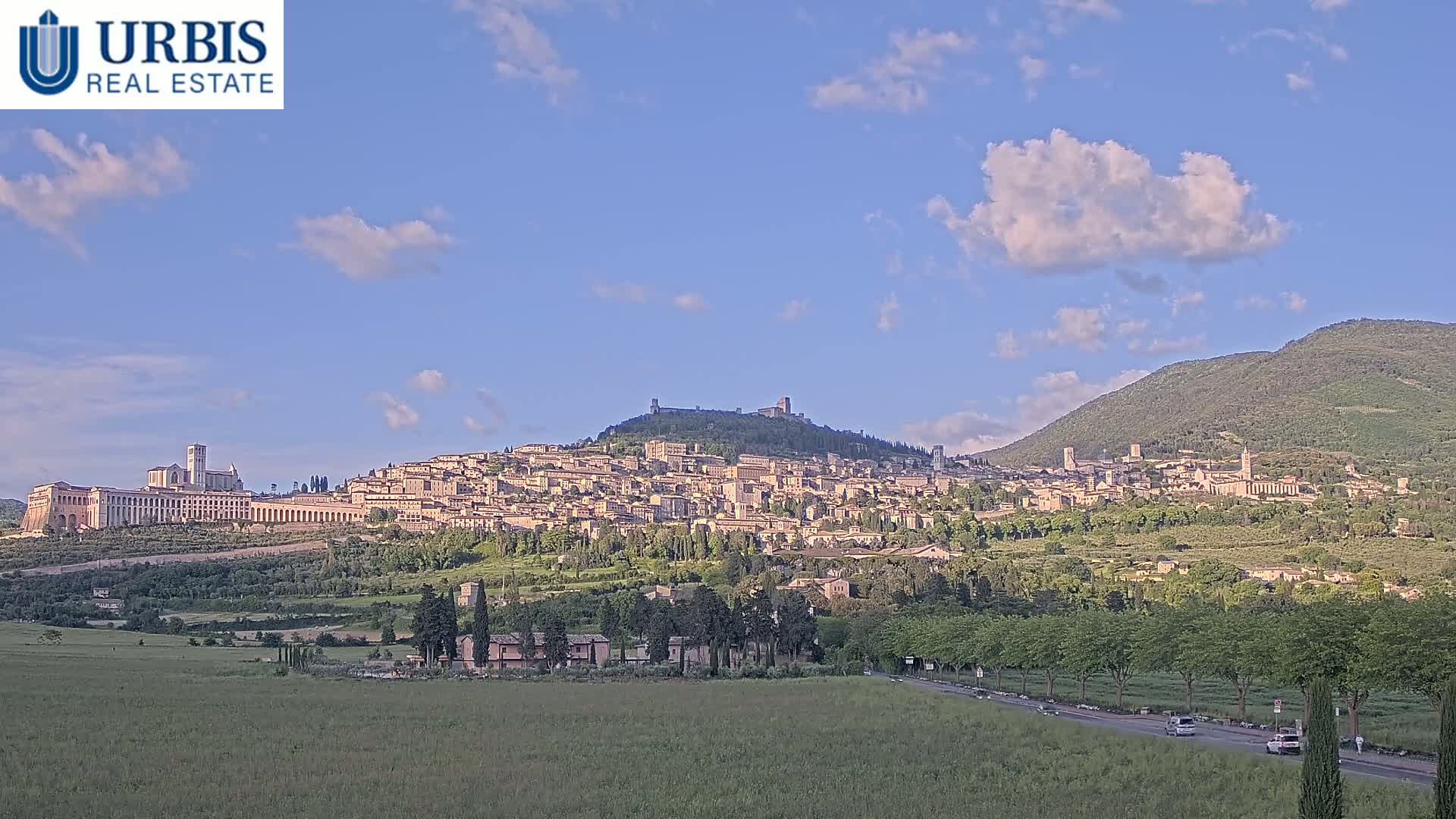 A hilltop town with many buildings, including a large basilica, is visible under a partly cloudy sky.