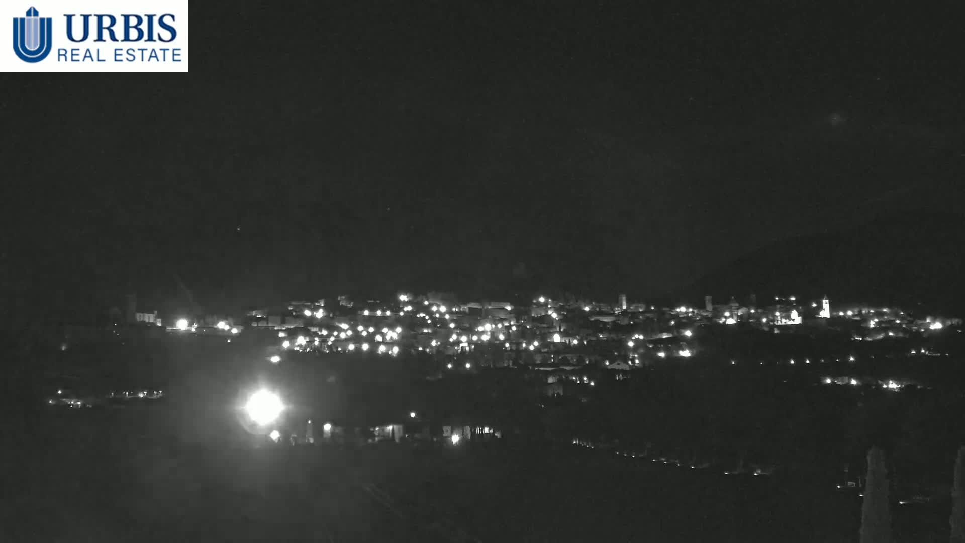 A nighttime, long-distance view shows a small town illuminated by scattered lights, nestled in a dark landscape.