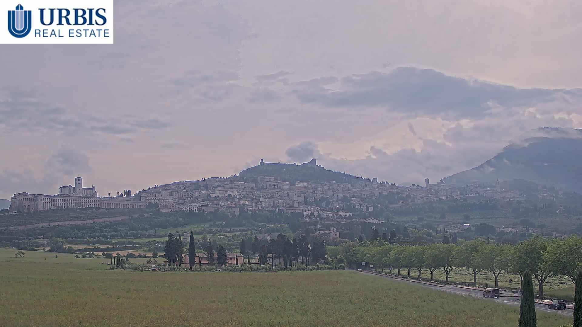 A hilltop town, nestled amongst rolling green hills and under a cloudy sky, is visible from a distance.