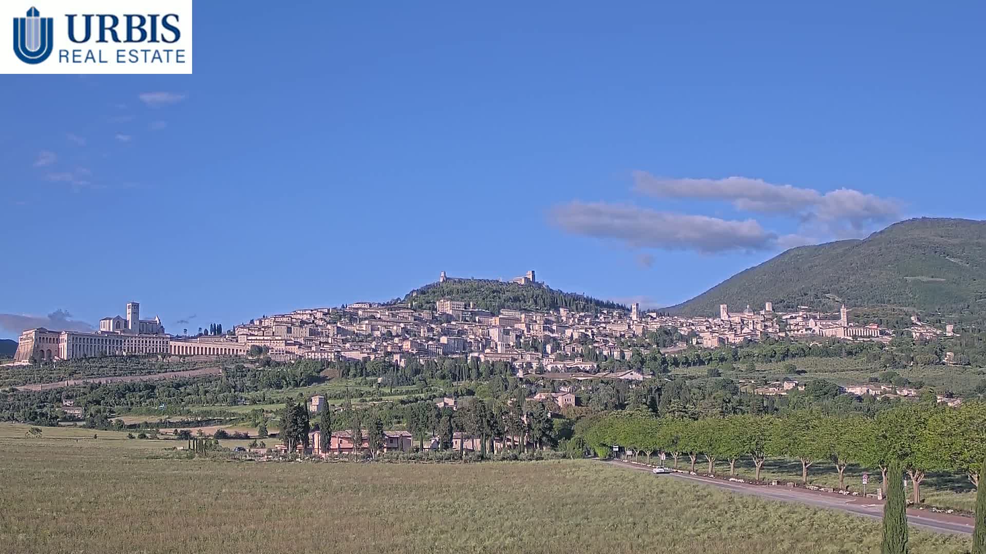 A hilltop town, nestled in a valley, is visible under a mostly clear blue sky with a few scattered clouds.