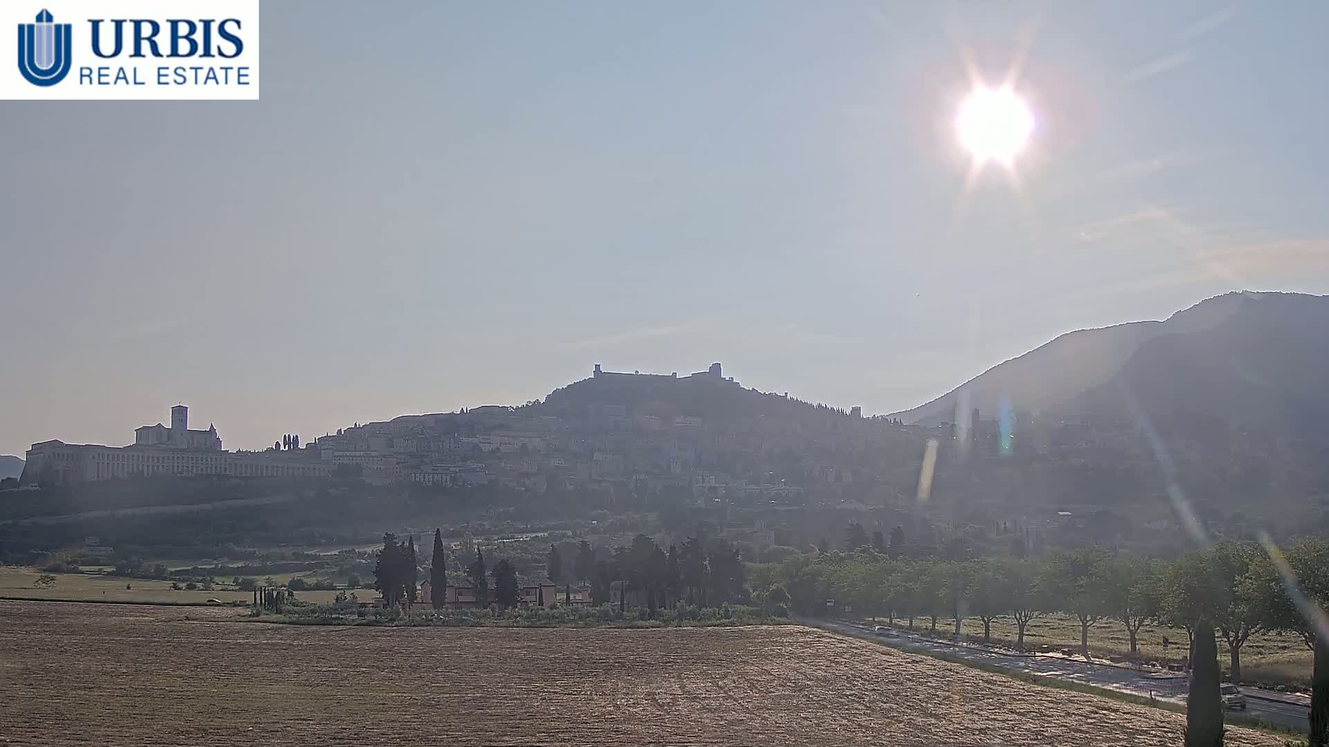 A hazy, sunny day reveals a distant hilltop town, its buildings and a large structure atop the hill barely visible through the atmospheric haze.