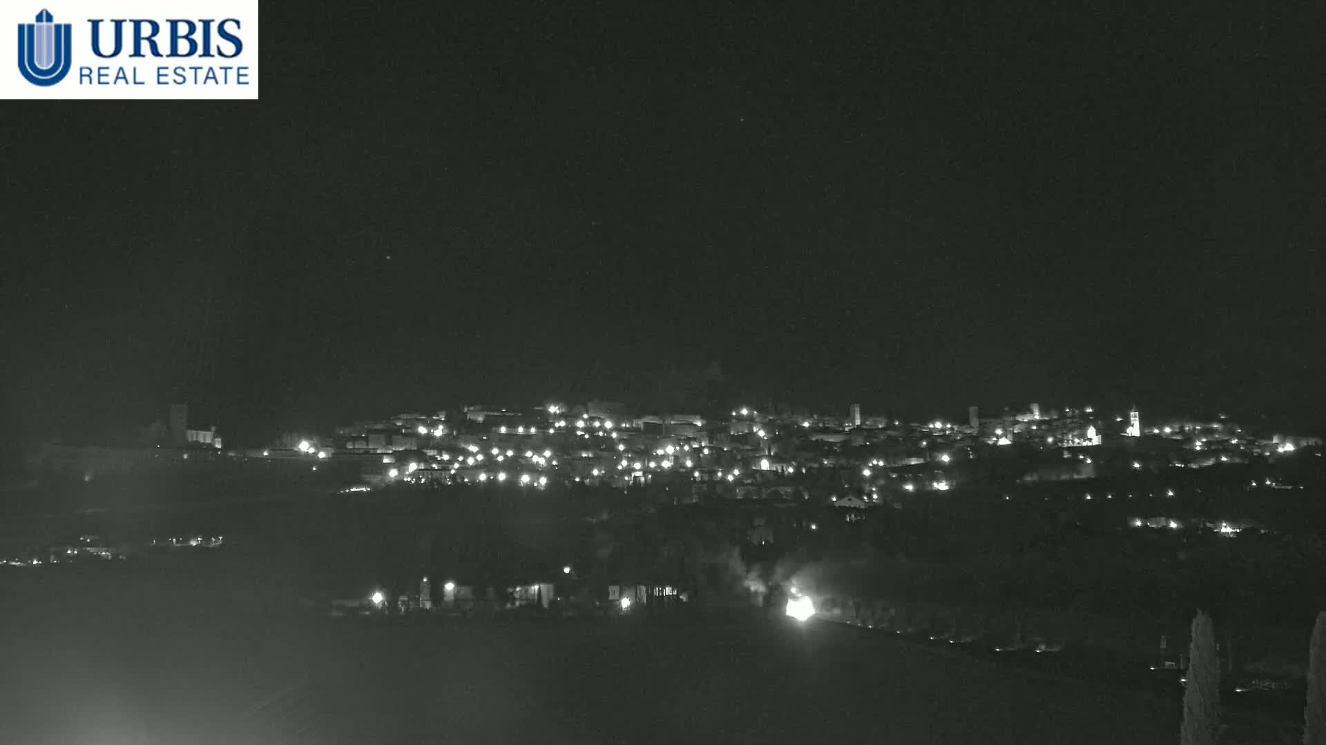A nighttime, long-range view of a small town illuminated by many lights, situated on a hill under a clear, dark sky.