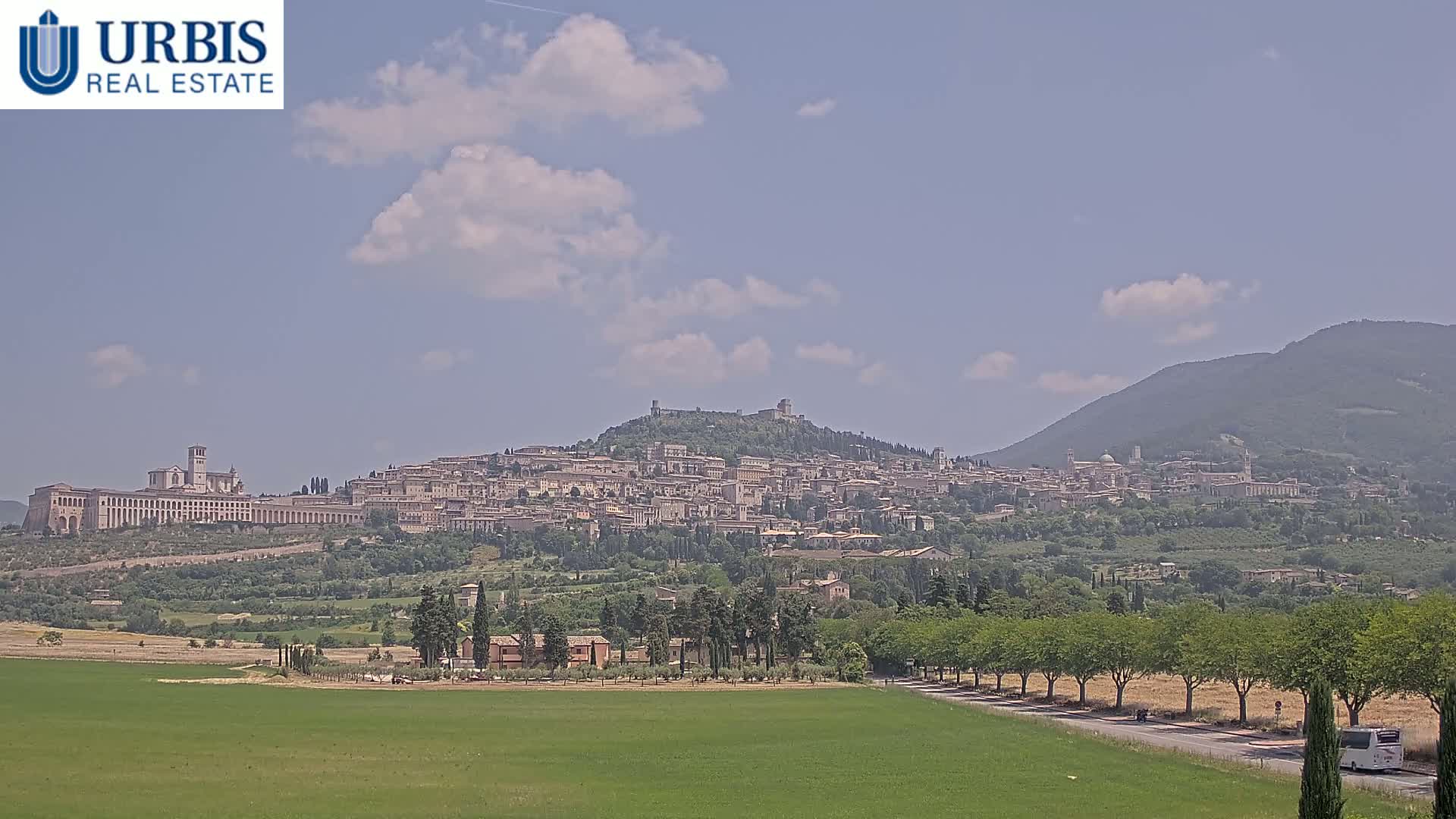 A large hilltop town, under a partly cloudy sky, is visible from a grassy field in the foreground.