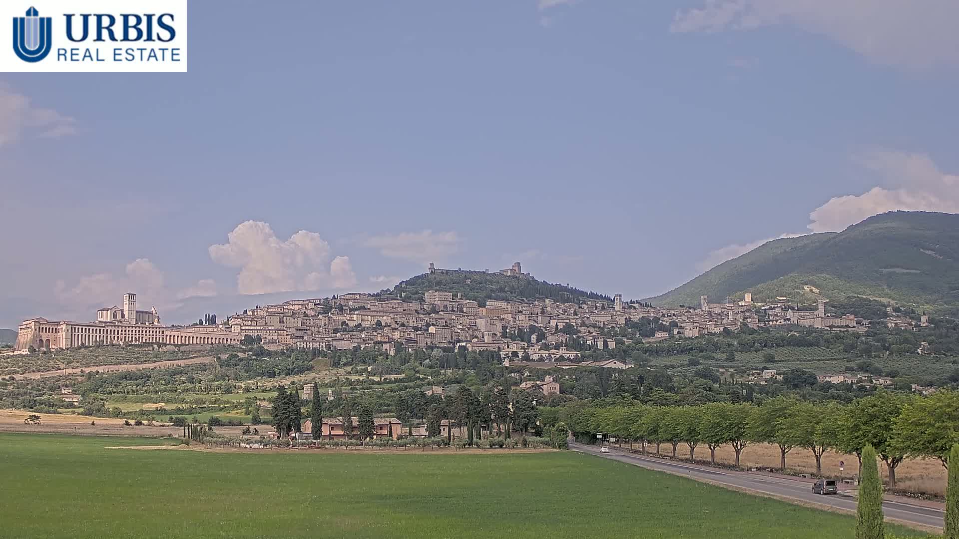 A large hilltop town, with a large basilica at its base, is visible under a partly cloudy sky.