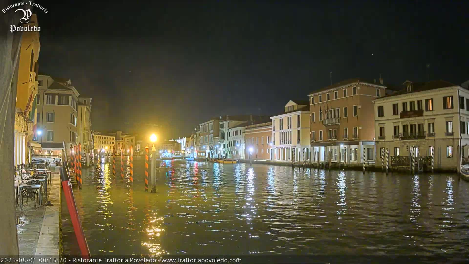 A calm canal at night reflects the lights of buildings lining its banks.