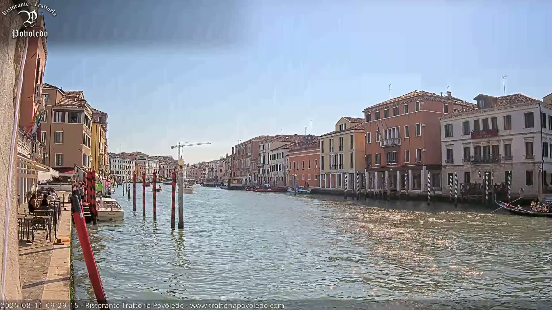 A Venetian canal on a sunny day, lined with colorful buildings, boats, and people sitting at an outdoor cafe.