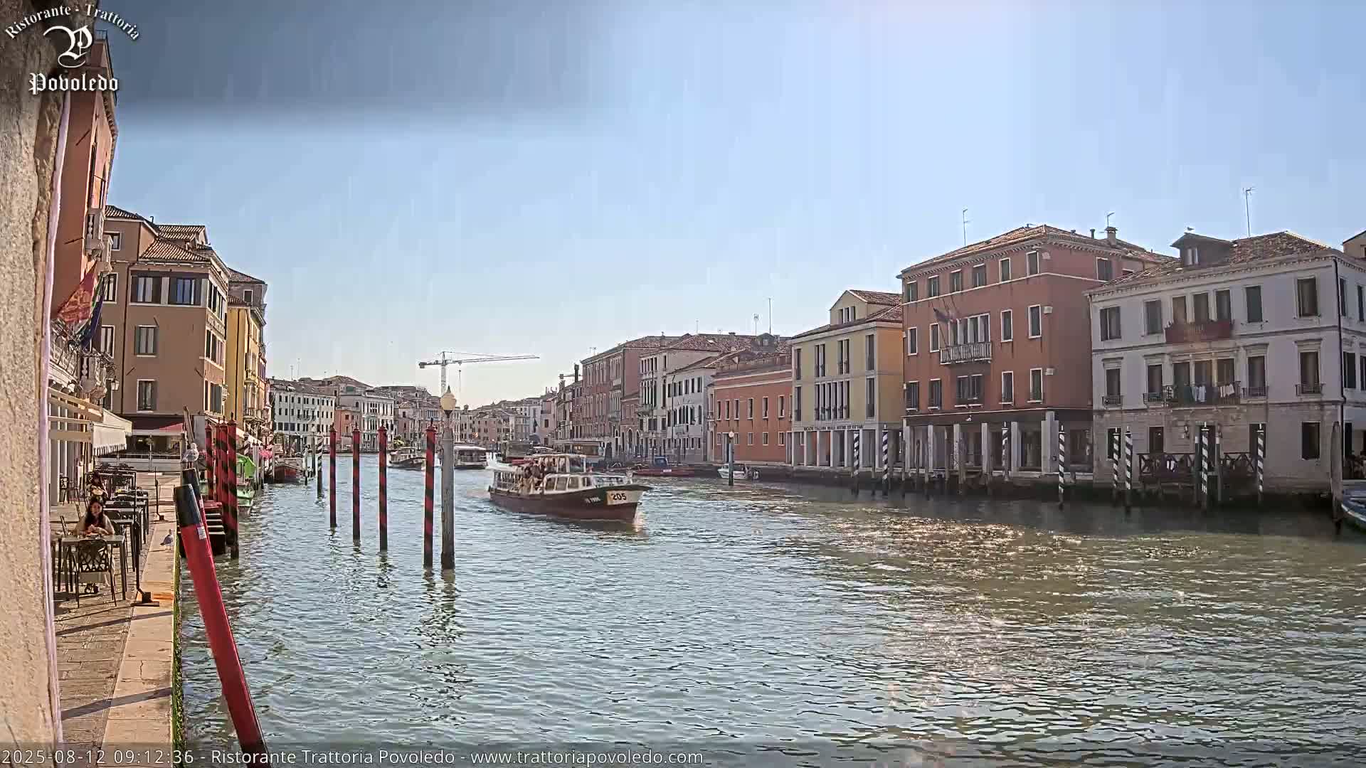A canal in Venice, under a clear sky, is lined with colorful buildings, and a boat is traveling down the waterway.