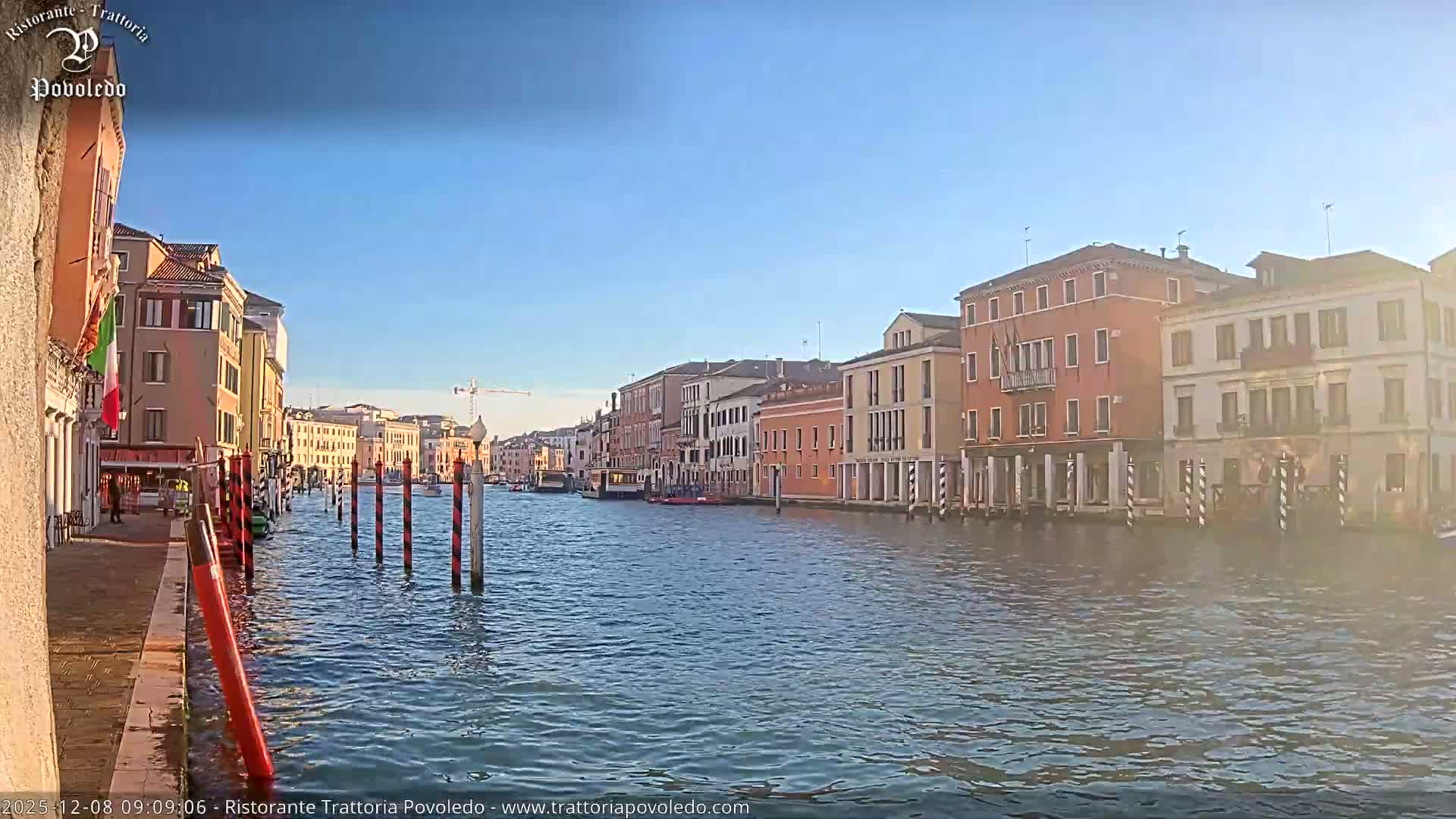 The image captures a sunlit canal, likely in Venice, bordered by an array of colorful historic buildings under a clear blue sky.