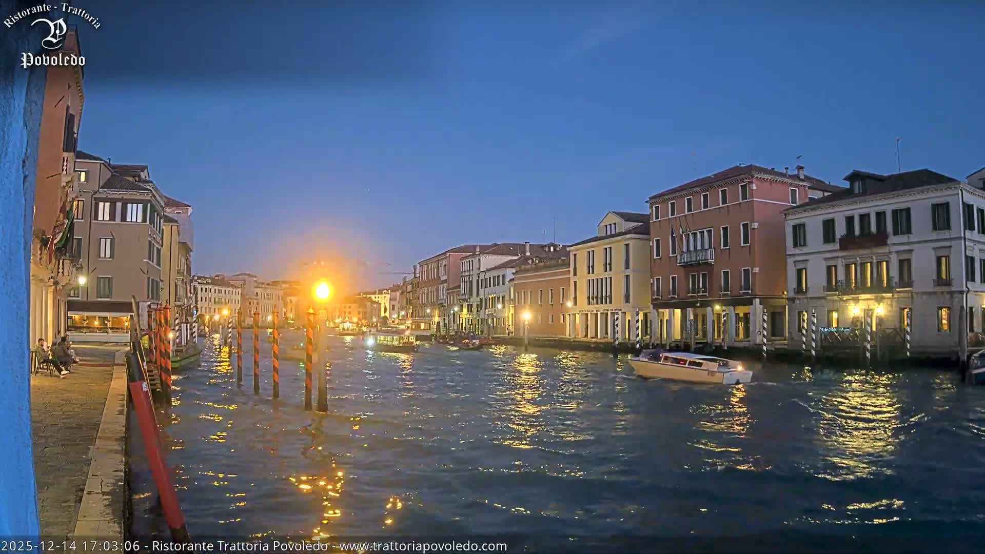The image captures a sunlit canal, likely in Venice, bordered by an array of colorful historic buildings under a clear blue sky.