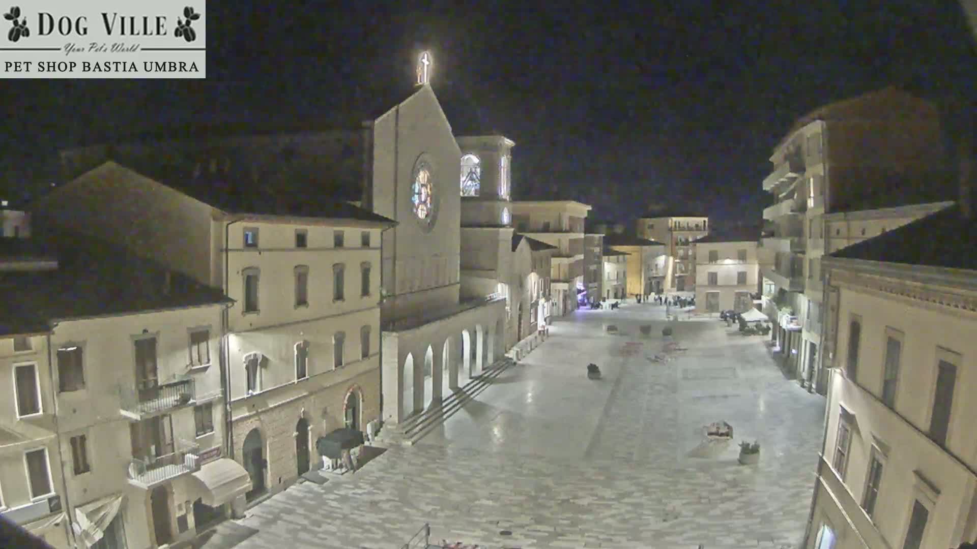 A nighttime view of a town square with a church and several buildings surrounding it under a clear, dark sky.