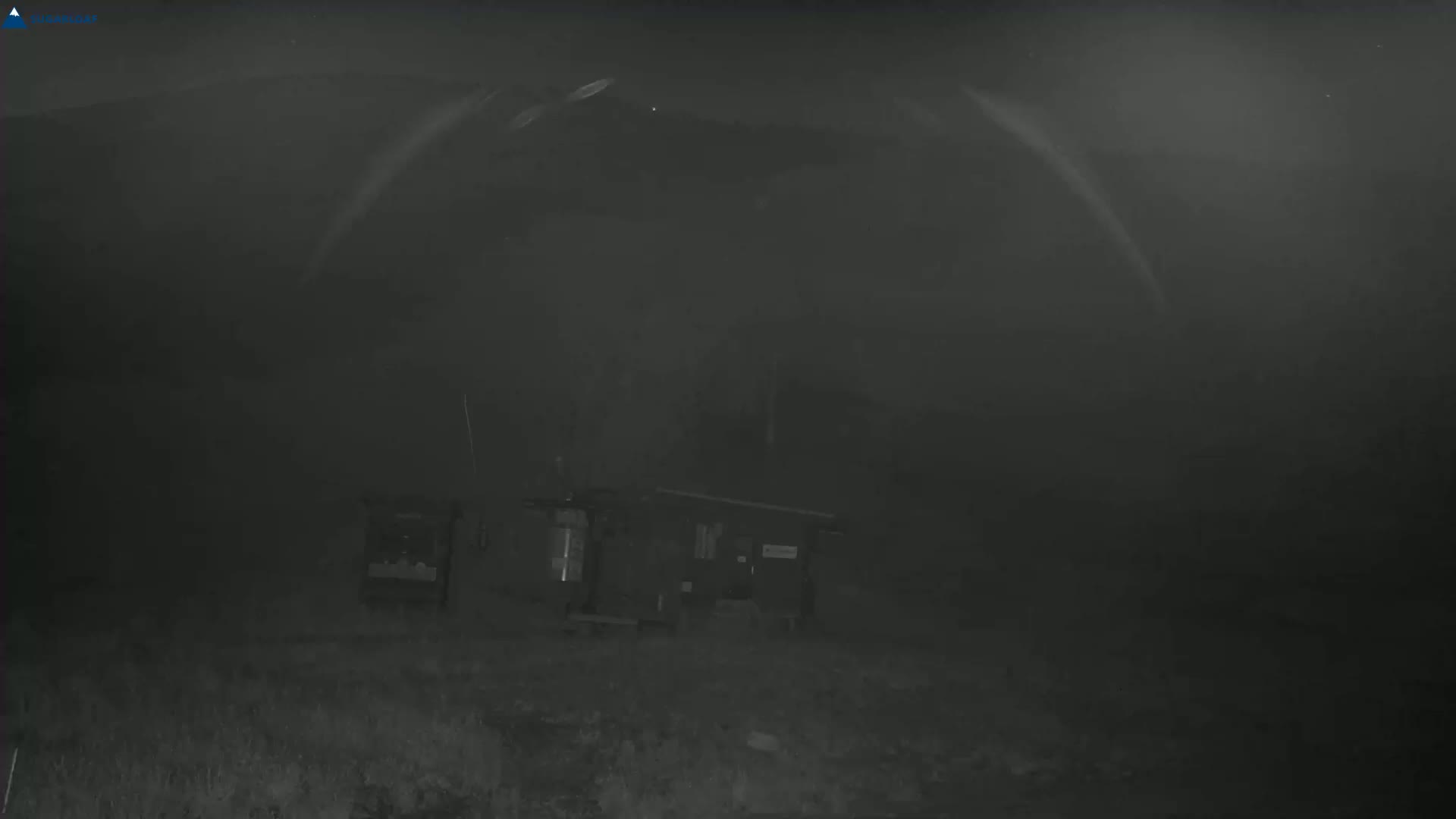A nighttime, foggy scene shows several dark objects, possibly equipment, situated on uneven ground.