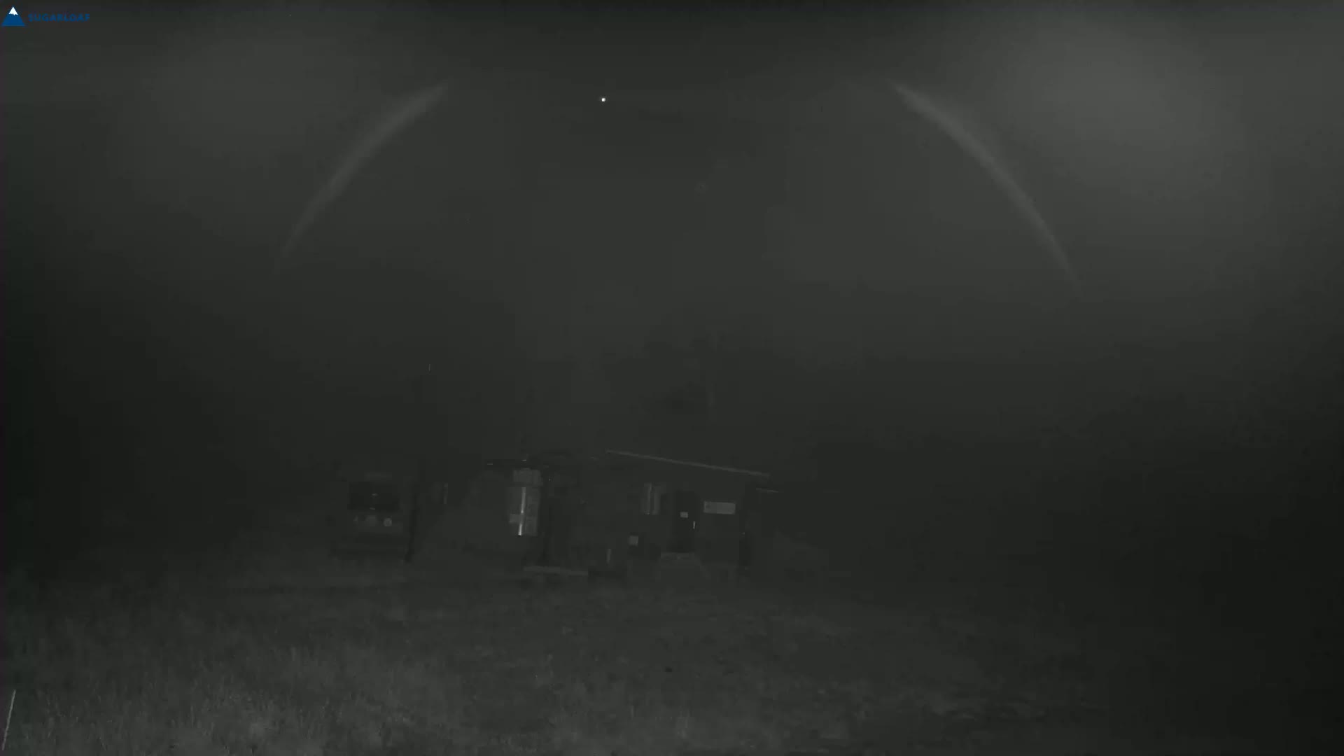 A small building is visible in the distance under a dark, foggy sky with a single bright light in the upper center.