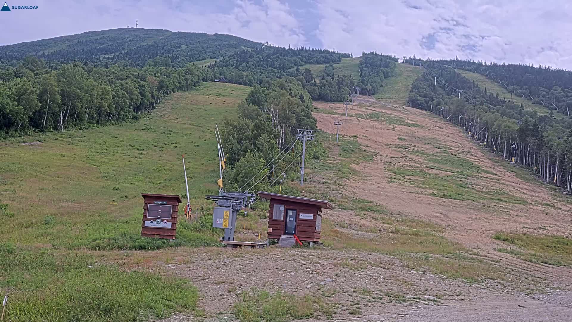 A ski lift and small building sit at the base of a grassy, mostly barren mountainside under a cloudy sky.